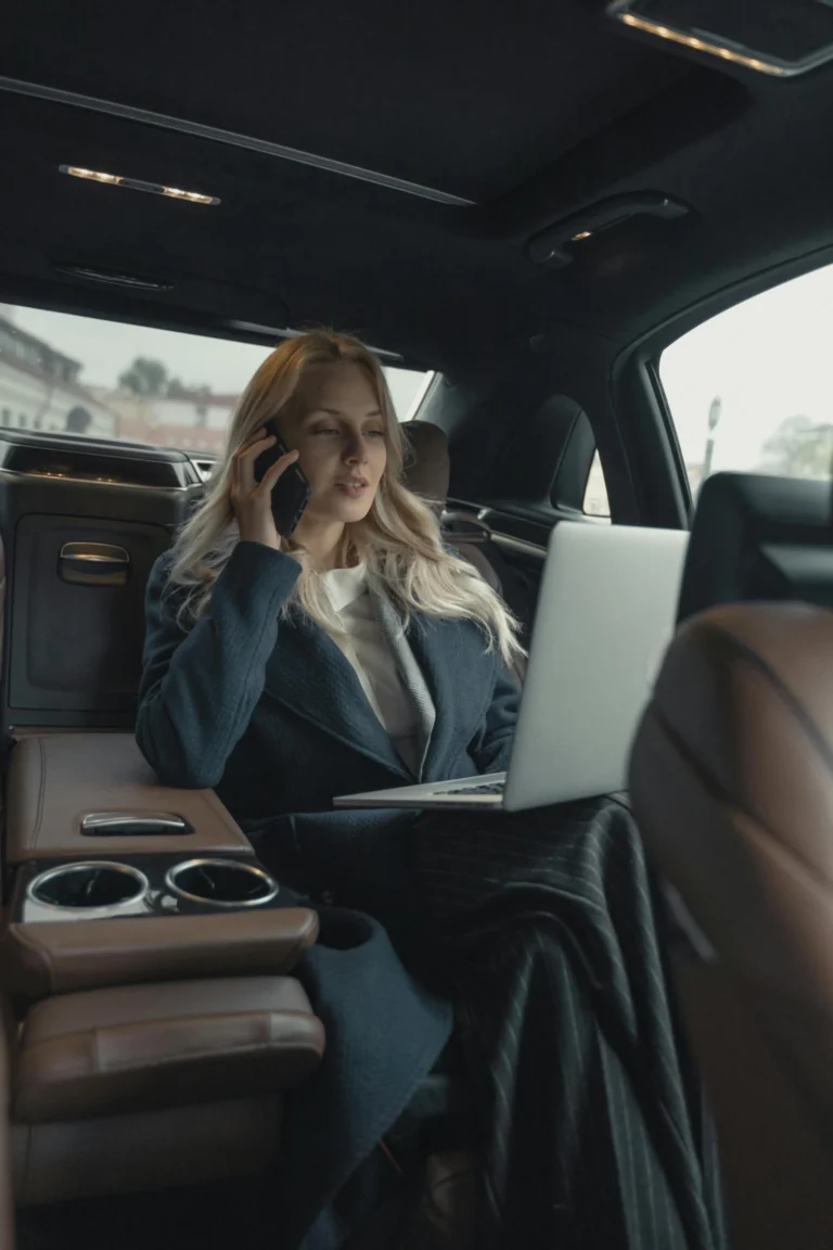 Limo service Sarasota Confident businesswoman making a call and working on a laptop in a luxury car interior.